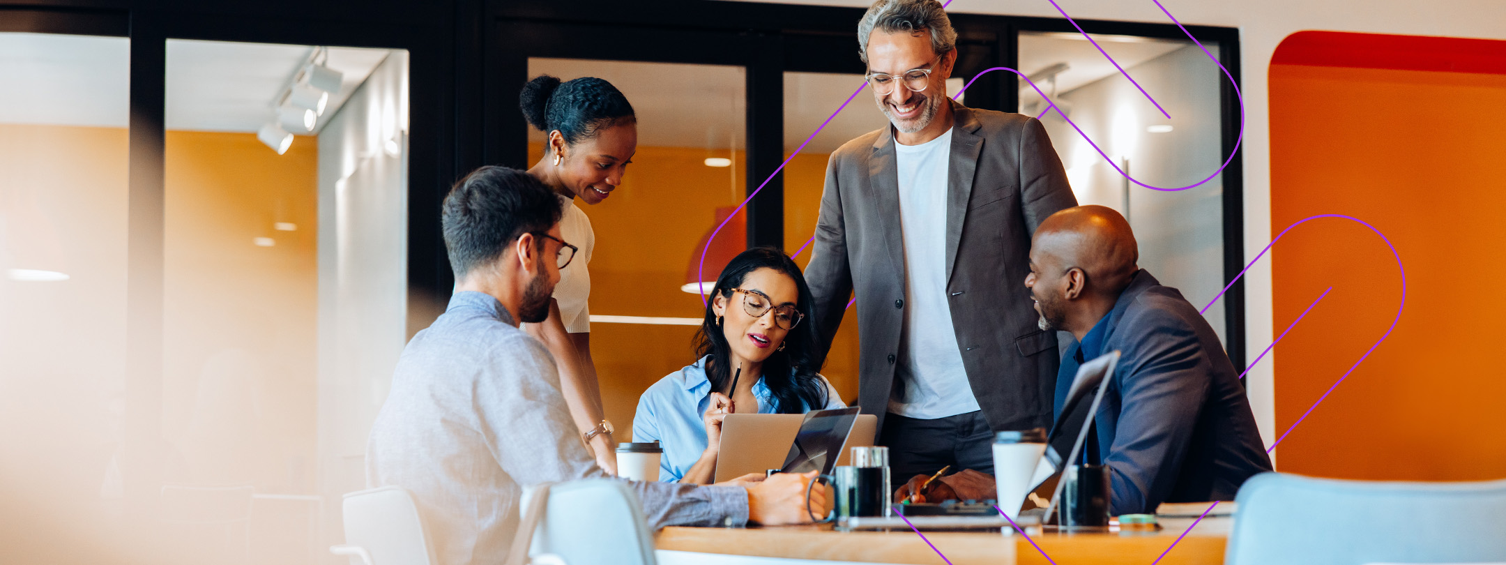 Group of employees at a conference table reviewing notes on a laptop.