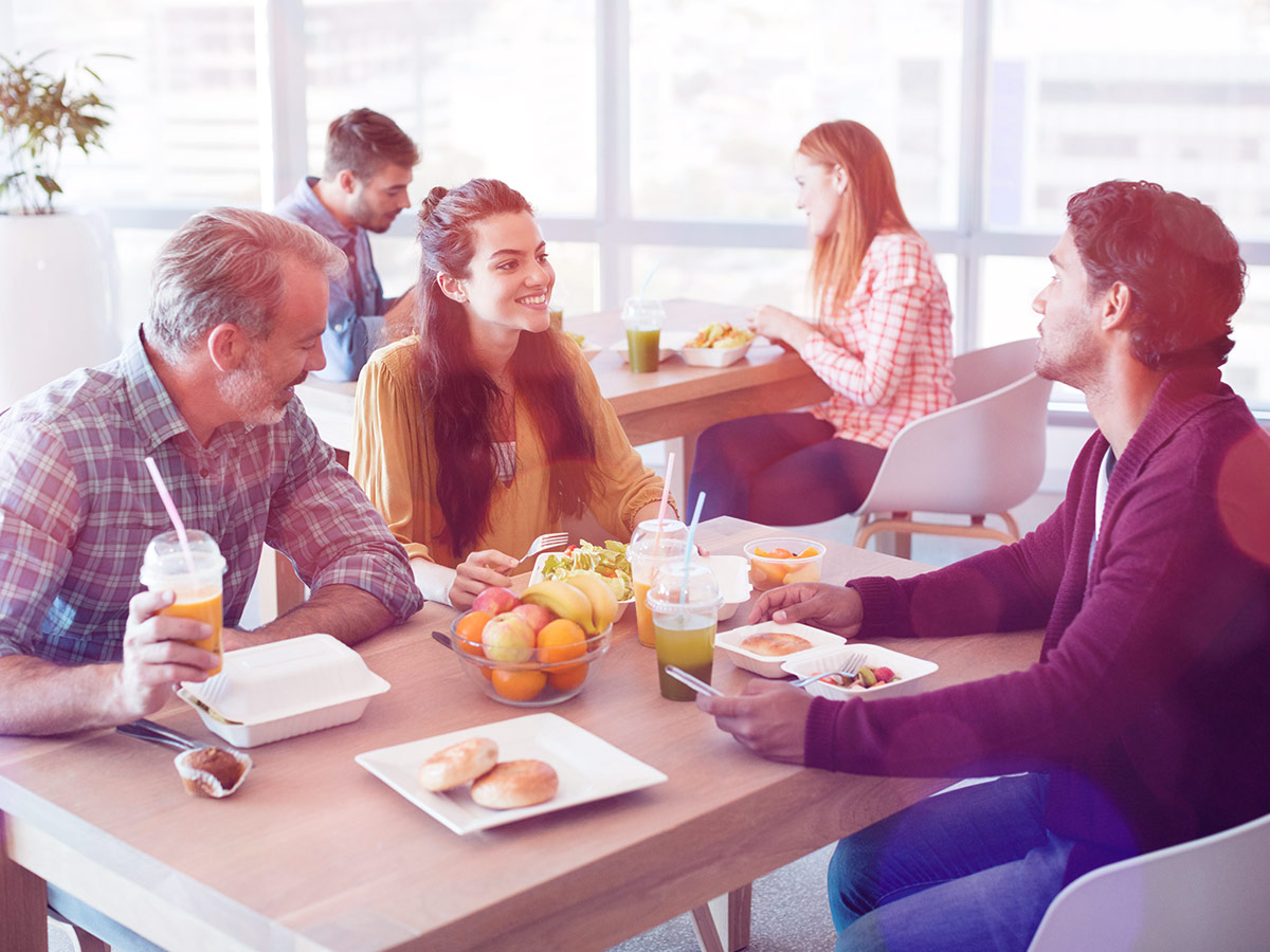 A photo of a group of coworkers smiling chatting while eating a healthy breakfast at work