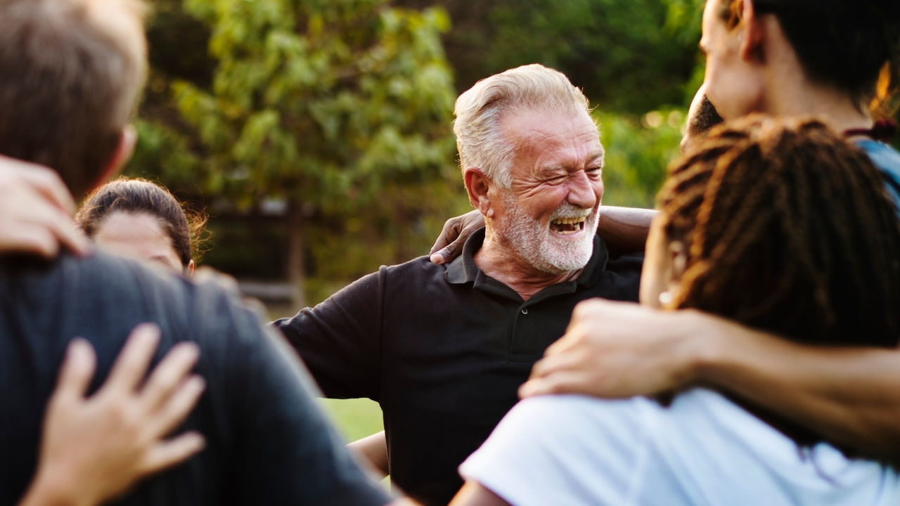 elder man in group hug surrounded by other people